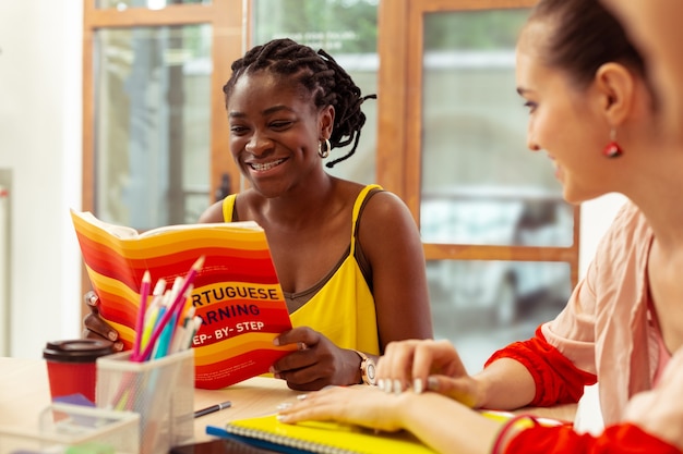 Live and learn. Cute brunette female keeping smile on her face while reading book in group