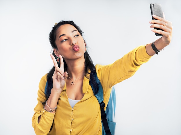 Live for the moments you cant put into words Studio shot of a woman wearing a backpack and taking selfies against a white background