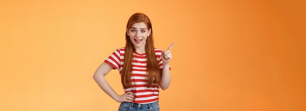 Lively friendly redhead woman discuss new trend pointing upper left corner smiling talking joyfully 