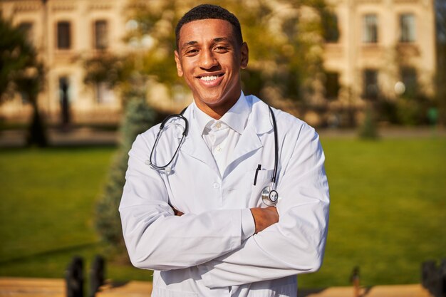 lively physician without a mask crossing his arms in a hospital courtyard