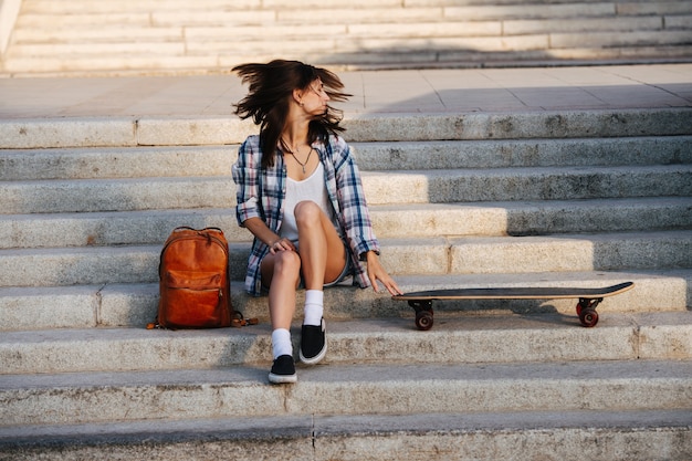 Foto donna vivace seduta sulle scale accanto al suo skateboard scuotendo la testa