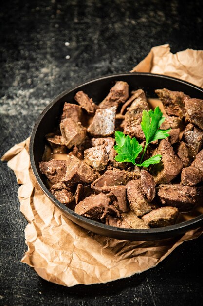 Liver in a frying pan on paper with a sprig of parsley