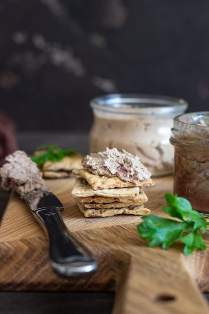 Liver pate in a glass jar with multigrain crackers and parsley.