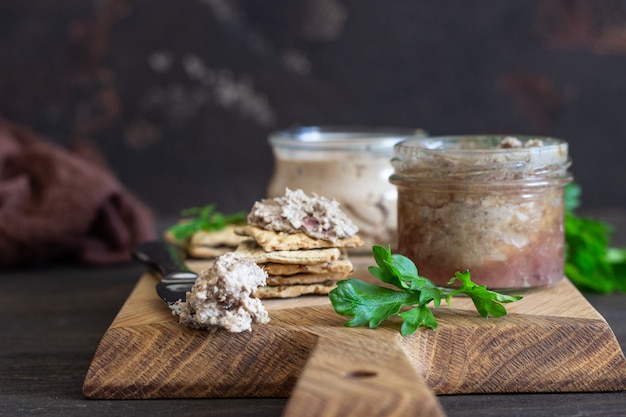 Liver pate in a glass jar with multigrain crackers and parsley.