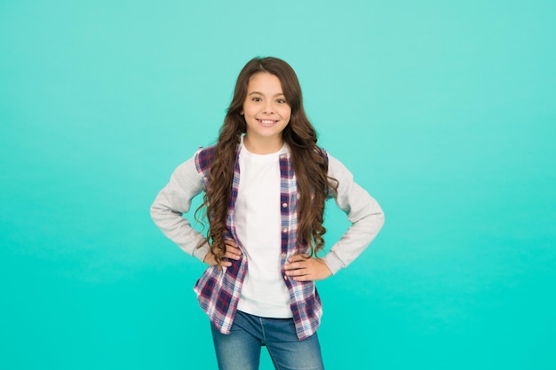 Living happy life Cute girl with long hair Small girl checkered shirt Happy international childrens day Little girl turquoise background Good mood concept Positive vibes Sincere emotions