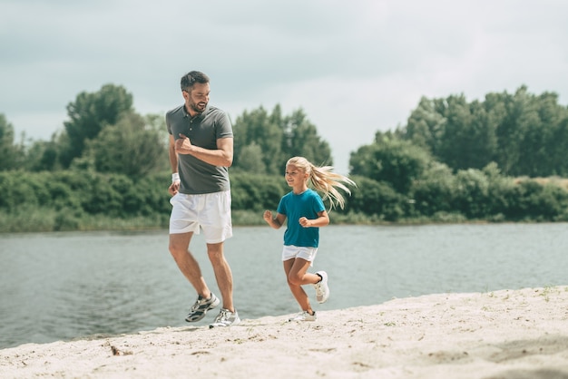 Living a healthy life. Full length of cheerful father and daughter in sports clothes jogging at the riverbank together