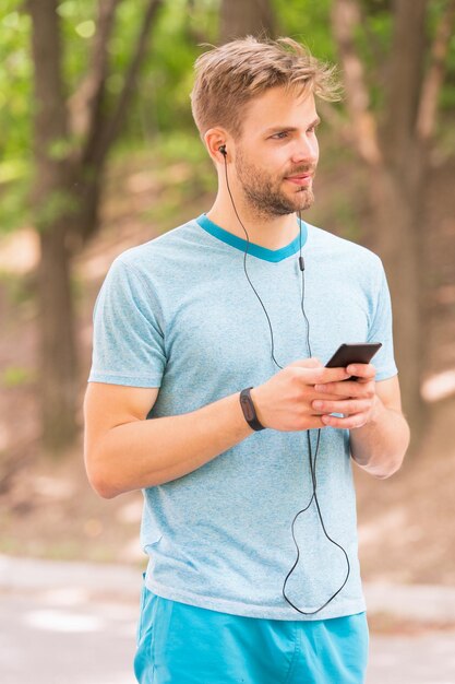 モバイルライフスタイルを生きるアスレチックマンが携帯電話アプリで自分の活動を追跡しますスポーツマンがモバイルデバイスとフィットネスウォッチを使用してトレーニングしますFitguyがモバイルインターネットを介してfitbitデータを同期します