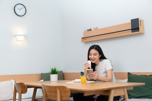 Living room concept a female adult enjoying eating sandwiches and orange juice watching online media in the work break.