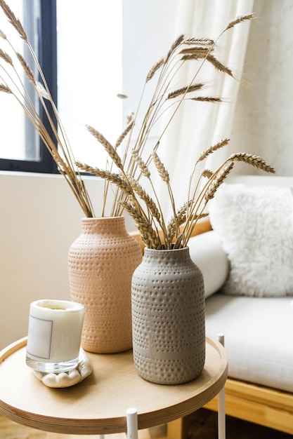 リビングルームの装飾 居心地の良い明るいソファの横にある木製のテーブルの上に、セラミック製の花瓶に乾燥小麦が置かれています