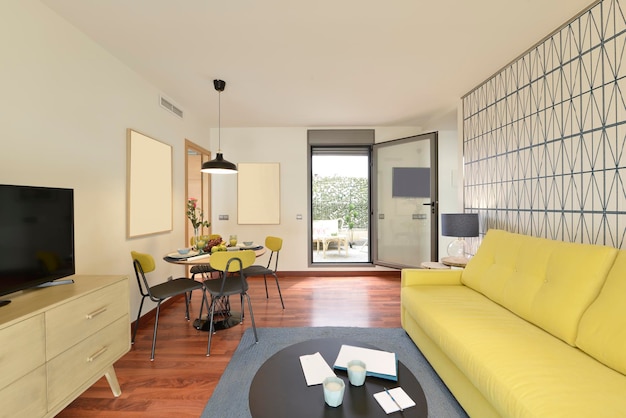 Living room of a house with a yellow threeseater sofa and access to a terrace with a glass door