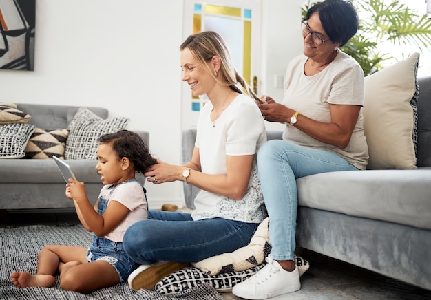 Living room mother and daughter to braid hair generations and bonding with love care or sitting on carpet Mom grandmother and child with hairdresser tablet or play games on floor in family home