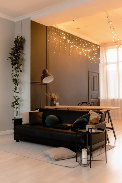 A living room with a black sofa and a white table with a string of lights hanging from it.