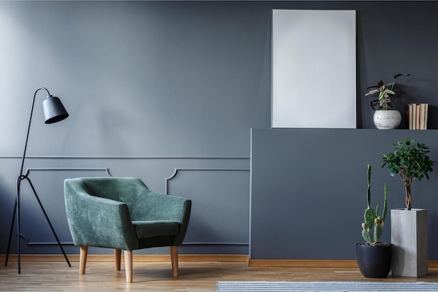 A living room with a gray wall and a green armchair in front of a plant.