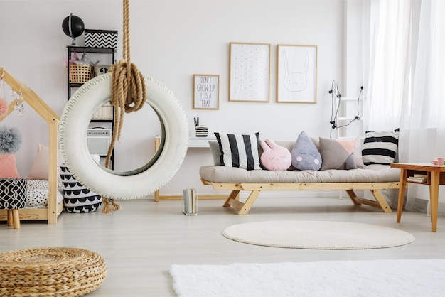 A living room with a swing hanging from the ceiling and a couch with pillows on it.