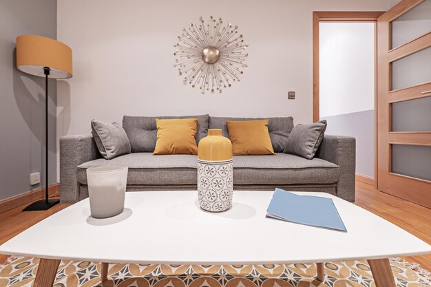 Living room with a threeseater sofa bed upholstered in gray fabric a white coffee table with a white and orange vase and yellow cushions