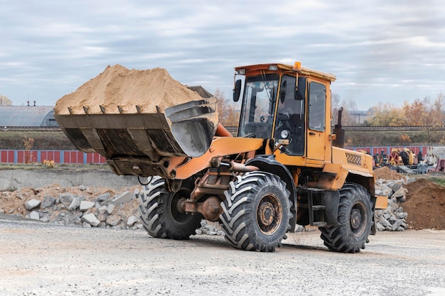 The loader is transporting sand or gravel in the front bucket. Heavy construction equipment at a construction site. Transportation of bulk materials in a concrete plant.