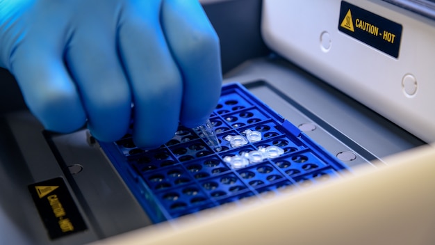 Loading a DNA tube into a PCR (polymerase chain reaction) thermocycler machine in a bioscience laboratory. Concept of science, laboratory and study of diseases.