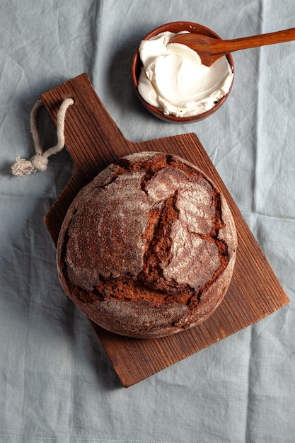 Loaf of artisan dark unleavened bread with cottage cheese searved on cutting board blue linen background