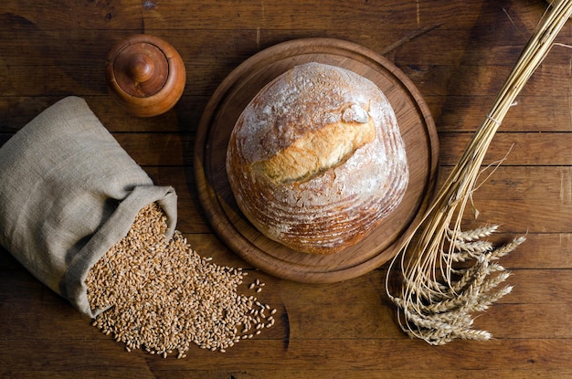 Loaf bread, spikelets and small bag with wheat grains on a\
wooden table. rustic style. top view.