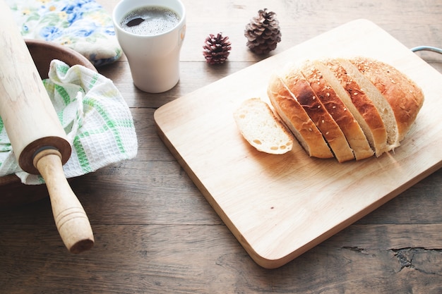 loaf of bread on wood background with cup of coffee and bakery tools, food closeup