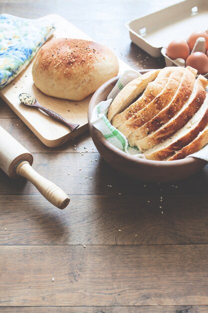 loaf of bread on wood background with eggs and bakey tools with