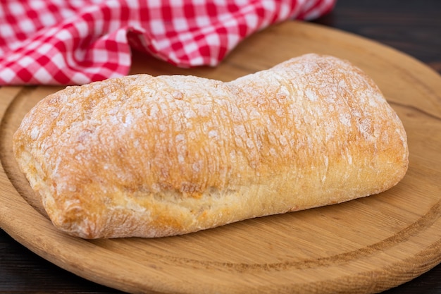 Loaf of ciabatta bread on a cutting board on the dark wooden table.