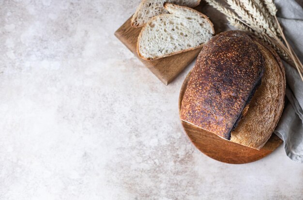 Loaf of fresh homemade sourdough bread on wooden plate with wheat ears