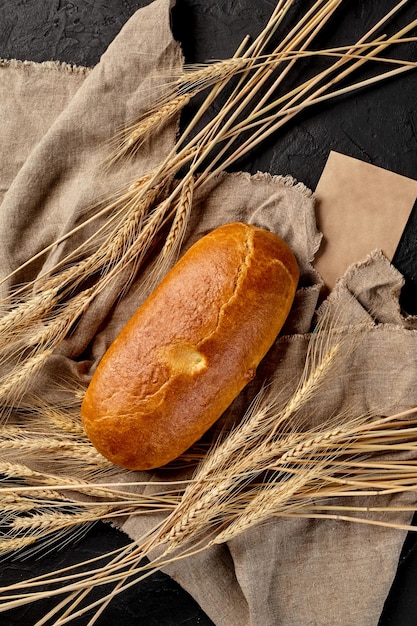 Буханка свежеиспеченного хлеба на срезе мешковины с колосьями пшеницы на черном фоне