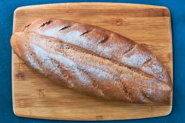 Loaf of freshly baked white bread on wooden board close up