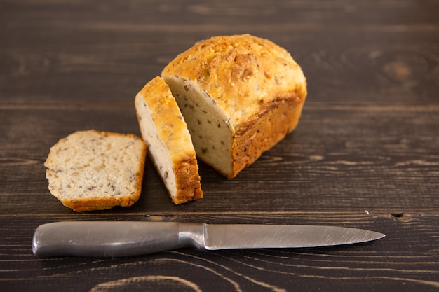 A loaf of sliced wholegrain bread on a wooden background next to a knife