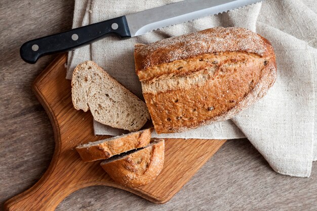 Loaf of whole wheat bread with slices on wooden board on kitchen table