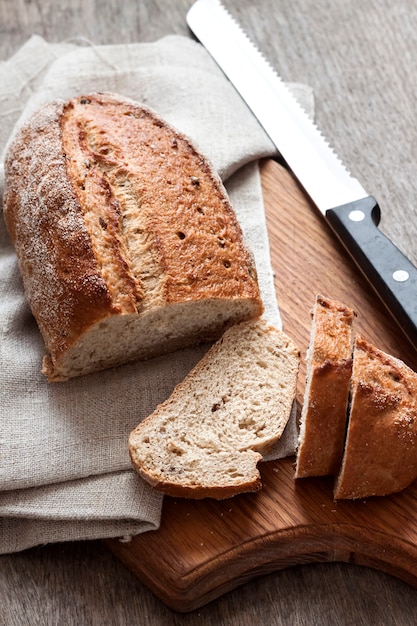 Буханка хлеба из цельной пшеницы с ломтиками на деревянной доске
