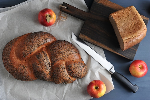 Буханка с маком и половина хлеба взятого крупным планом с яблоками и ножом