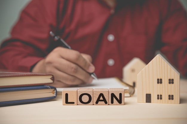 LOAN on wood blocks with house model Concept loan buy house banking financial accounting insurance A businessman recording expenses and calculates debt payments home loans and other expenses