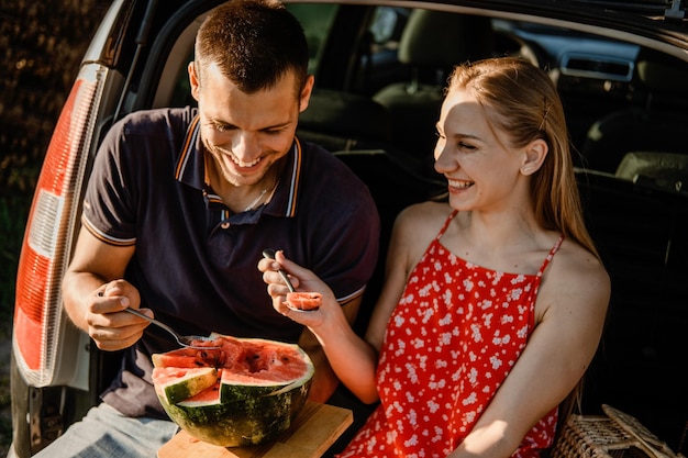 車のトランクにスイカと夏のピクニックで恋に地元の旅行ロマンチックなピクニックの日付のアイデアのカップル