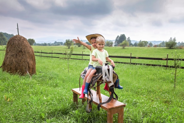 Foto vacanza locale, stai al sicuro, resta a casa. bambini piccoli in cappello da cowboy che giocano in western nella fattoria tra le montagne, felice estate in campagna, infanzia e sogni