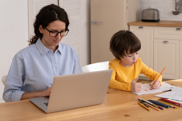 Lockdown familie afstand baan kind schilderen terwijl zijn moeder op laptop thuis kantoor werkt