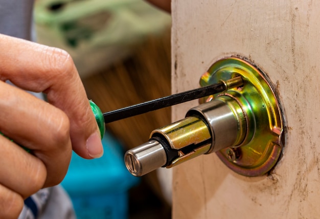 Photo the locksmith is repairing the wooden door knob with screwdriver.