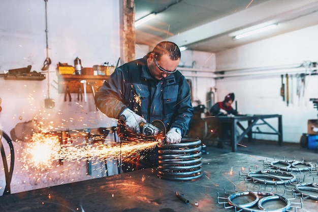 Locksmith in special clothes and goggles works in production metal processing with angle grinder spa