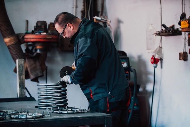 Locksmith in special clothes and goggles works in production metal processing with angle grinder spa