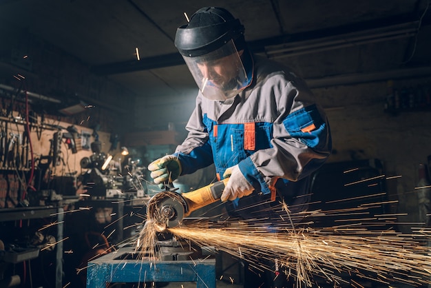 Locksmith in special clothes and goggles works in production. Metal processing with angle grinder. Sparks in metalworking.