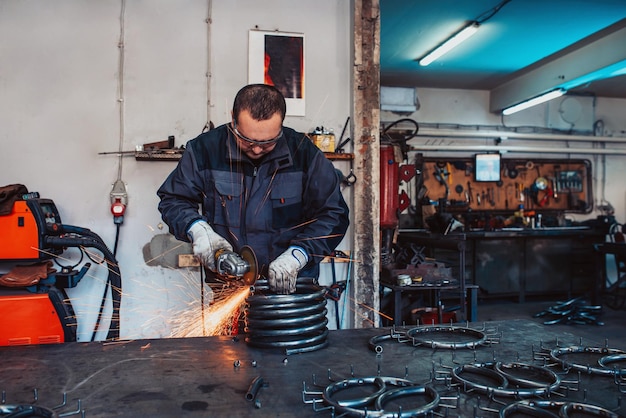 Locksmith in special clothes and goggles works in production Metal processing with angle grinder Sparks in metalworking