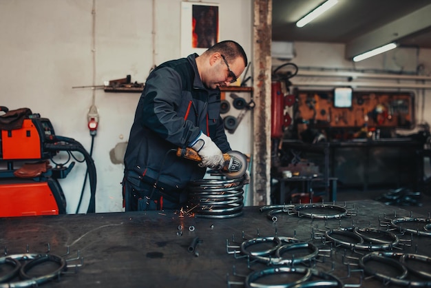 Слесарь в специальной одежде и очках работает на производстве Обработка металла угловой шлифовальной машиной Искры в металлообработке