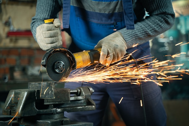 Locksmith in special clothes and goggles works in production. Metal processing with angle grinder