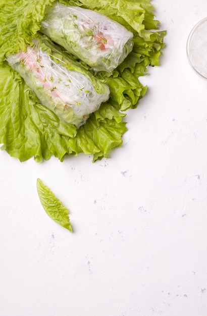 Loempia's van groenten op groene bladeren op wit. Bij de noedels met kopie ruimte. Vegetarisch gerecht