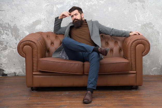 Loft interieur appartement. Zakenman makelaar werk. Meubel winkel. Hipster makelaar in loft-stijl appartement. Makelaar en verhuurservice. Huur appartement. Bebaarde man met zelfverzekerd gezicht zit op een leren bank.