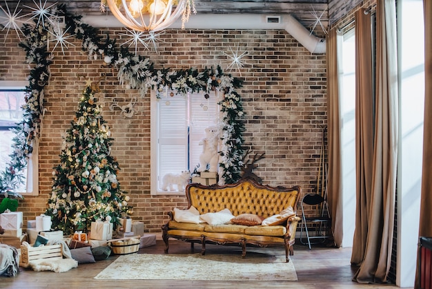 La camera in stile loft è decorata con decorazioni di capodanno. divano in pelle vintage di lusso e albero di natale.