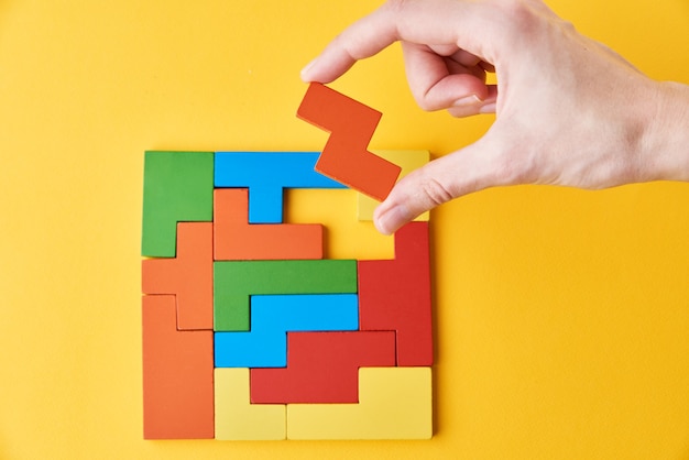 Logical thinking and finishing task concept. Woman hand adding last missing wooden block to finish a puzzle