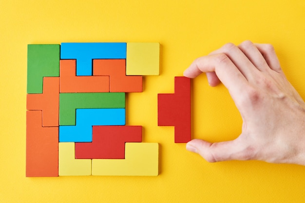 Logical thinking and finishing task concept. Woman hand adding last missing wooden block to finish a puzzle