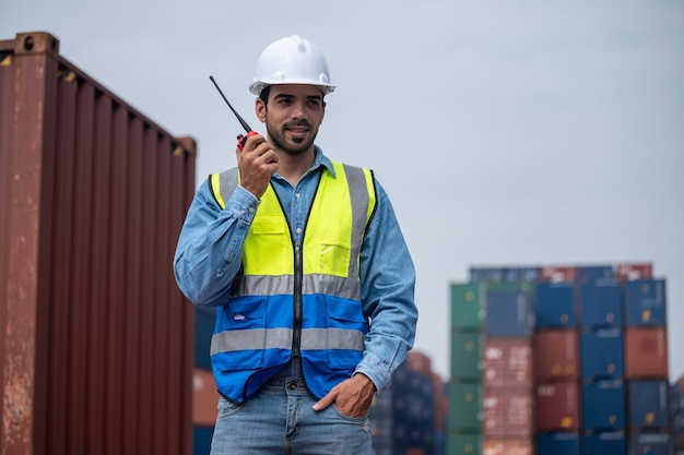 Logistic manager talking on the walkietalkie at container
warehouse for control loading containers in container yard terminal
shipping worker container talking radio to manage the export of
goods